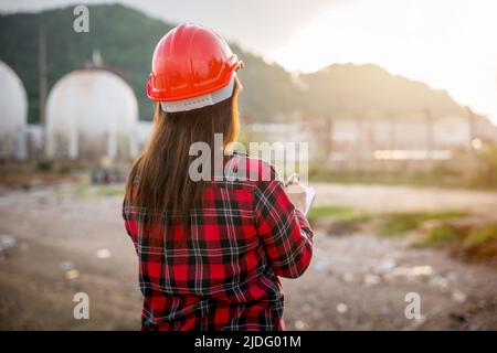 Erdölingenieure. Glückliche asiatische Arbeiterin Frau in der Ölindustrie Chemieindustrie Arbeiter arbeitet visuelle Inspektionsliste auf Zwischenablage im Werk, tun Aktion der Arbeit Stockfoto