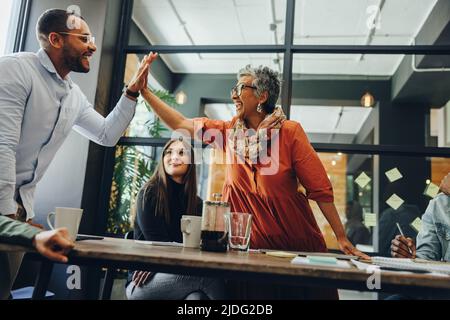 Fröhliche Geschäftskollegen, die sich während eines Büromeeting gegenseitig hoch fiving. Erfolgreiche Geschäftsleute feiern ihre Leistung. Glückliches Geschäft Stockfoto