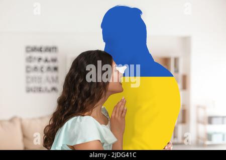 Junge Frau und Silhouette des Mannes in den Farben der ukrainischen Flagge zu Hause Stockfoto