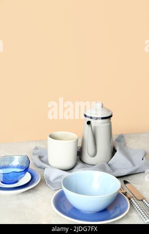 Elegantes Setting mit Tellern, Tasse und Teekannen auf grauem Tisch vor beigefarbenem Hintergrund Stockfoto