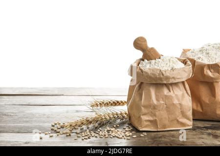 Papiertüten mit Mehl, Schaufel und Weizenohren auf Holztisch vor weißem Hintergrund Stockfoto