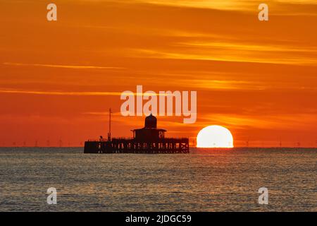 Herne Bay, Kent, Großbritannien. 21.. Juni 2022: Wetter in Großbritannien. Sonnenaufgang an der Sommersonnenwende in Herne Bay in Kent, mit dem alten Pier Kopf, der gegen den morgendlichen orangefarbenen Schein silhouettiert wird, während ein weiterer heller, sonniger und warmer Tag beginnt. Kredit: Alan Payton/Alamy Live Nachrichten Stockfoto