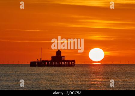 Herne Bay, Kent, Großbritannien. 21.. Juni 2022: Wetter in Großbritannien. Sonnenaufgang an der Sommersonnenwende in Herne Bay in Kent, mit dem alten Pier Kopf, der gegen den morgendlichen orangefarbenen Schein silhouettiert wird, während ein weiterer heller, sonniger und warmer Tag beginnt. Kredit: Alan Payton/Alamy Live Nachrichten Stockfoto