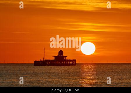 Herne Bay, Kent, Großbritannien. 21.. Juni 2022: Wetter in Großbritannien. Sonnenaufgang an der Sommersonnenwende in Herne Bay in Kent, mit dem alten Pier Kopf, der gegen den morgendlichen orangefarbenen Schein silhouettiert wird, während ein weiterer heller, sonniger und warmer Tag beginnt. Kredit: Alan Payton/Alamy Live Nachrichten Stockfoto