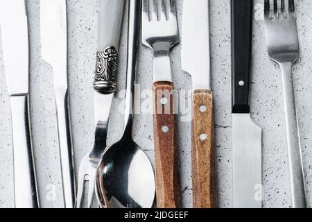 Nahaufnahme von Besteck auf einer Tischoberfläche. Messer, Gabeln und Löffel aus Edelstahl. Einige mit Holzgriffen. Nach oben und unten zeigen. Stockfoto