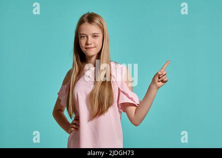 Studioportrait eines wunderschönen blonden Teenagers in einem rosa T-Shirt, das auf einem blauen Hintergrund posiert. Stockfoto