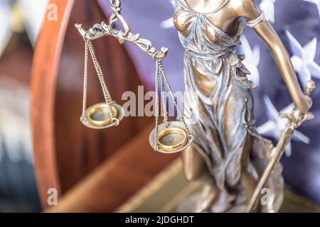 Bronzegigine von Themis hält Eheringe auf Waage und steht im Vordergrund. Ehescheidung. Stockfoto
