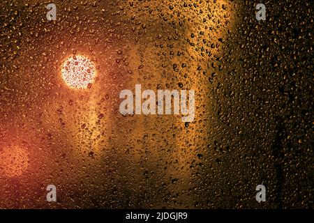 Wassertropfen auf einem Fenster mit Stadtlichtern im Hintergrund am Abend Stockfoto