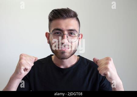 Teenager in der Siegerposition, Porträt eines kaukasischen hübschen Teenagers in der Siegerposition geballte Fäuste. Braunhaariger Teenager der Generation z. Stockfoto