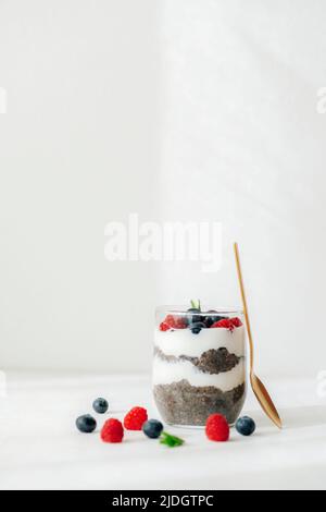 Glas Chia Pudding mit frischer Himbeere und Heidelbeere im Sonnenlicht auf weißem Tisch, Nahaufnahme. Stockfoto