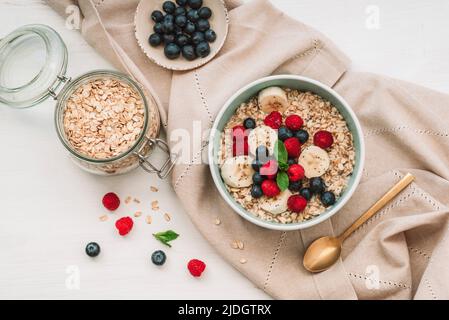 Hausgemachter Haferbrei mit Himbeeren, Heidelbeeren und Chiasamen auf weißem Tisch. Gesundes Frühstück. Draufsicht, flach liegend. Stockfoto