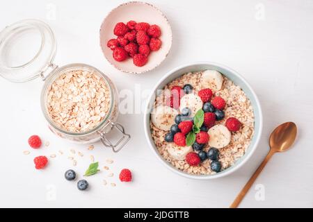 Hausgemachter Haferbrei mit Himbeeren, Heidelbeeren, Banane und Chiasamen auf weißem Tisch. Gesundes Frühstück. Draufsicht, flach liegend. Stockfoto