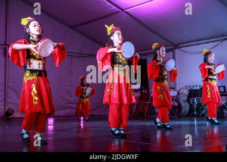 Junge asiatische Mädchen in bunten Volkstrachten tanzen auf der Bühne mit Tamburinen während der Mondfestlichkeiten. Auckland, Neuseeland Stockfoto