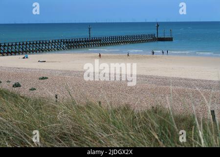 Littlempton, West Sussex, Großbritannien. Blick über die Sanddünen hinter dem West Beach. Zeigt Wellenbrecher am Eingang zum Fluss Arun. Windturbinen am Horizont. Stockfoto