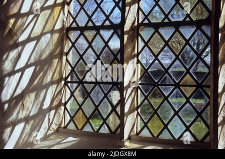 Detail eines Kirchenfensters mit Steinrahmen und diamantbedrahteten Scheiben aus klarem oder hellgelben Glas, die interessante Schatten werfen Stockfoto