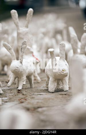 Weiße Kaninchenstatuen aus Gips bei der Kunstausstellung im Freien, künstliche weiße Hasen auf der Straße der Stadt. Viele weiße handgemachte Kaninchen, viele dekorativ Stockfoto