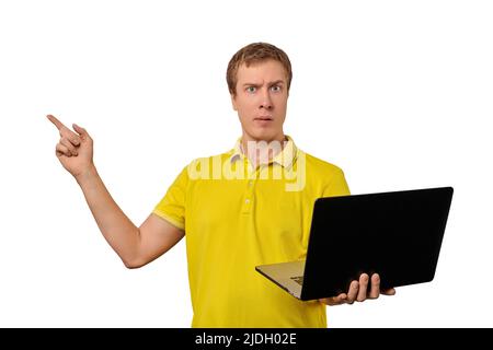 Rätselhafter junger Mann in gelber T-Short, der Laptop in einem schwarzen Gehäuse hält und mit einem Finger auf weißem Hintergrund zeigt. Witziger verwirrter Mann, der nicht hält Stockfoto