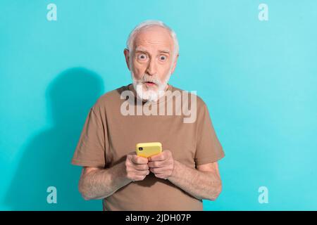 Portrait von attraktiven betäubt funky grauhaarigen Mann mit Gadget Wow Nachrichten Reaktion isoliert über hellen blauen Hintergrund Stockfoto