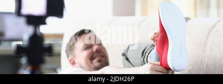 Männer mittleren Alters setzen sich trendige rote Sneaker an und zeigen sie vor der Kamera Stockfoto