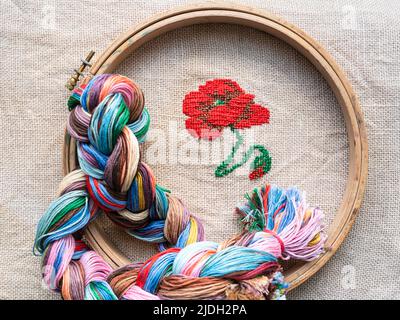 Draufsicht auf Moulingewirne aus Geflecht, Holzreifen und roter Mohnblume, die von Hand auf Leinwand gestickt wurden Stockfoto