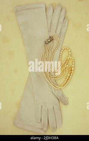 Paar Ellenbogenlang weißen Satin Damen Handschuhe leicht schmuddelig durch den Einsatz liegen auf antikem Papier mit dreireibigen Satz von Perlen Stockfoto