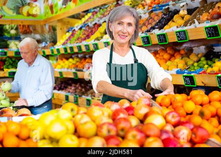 Weibliche Supermarktarbeiterin stapelt Früchte im Verkaufsraum auf dem Regal Stockfoto