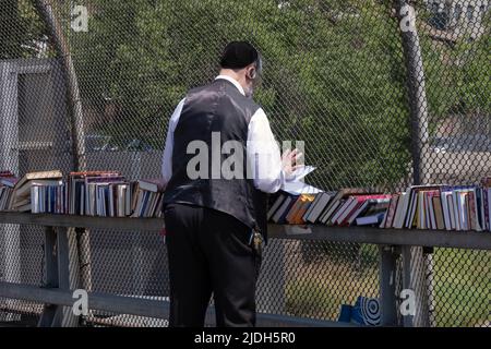 Ein anonymer orthodoxer jüdischer Mann stösst bei einem Verkauf religiöser Bücher im Freien nach. An der Lee Avenue in Williamsburg, Brooklyn, New York City. Stockfoto