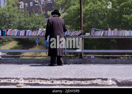 Ein anonymer orthodoxer jüdischer Mann stösst bei einem Verkauf religiöser Bücher im Freien nach. An der Lee Avenue in Williamsburg, Brooklyn, New York City. Stockfoto