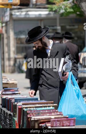 Ein jüdischer Mann, der bei einem Verkauf religiöser Bücher im Freien in schwarzen Augenbrauen gekleidet war. In Williamsburg, Brooklyn, New York. Stockfoto