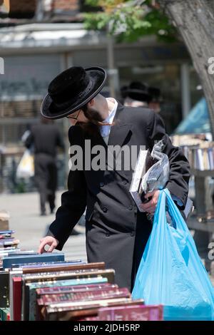 Ein jüdischer Mann, der bei einem Verkauf religiöser Bücher im Freien in schwarzen Augenbrauen gekleidet war. In Williamsburg, Brooklyn, New York. Stockfoto