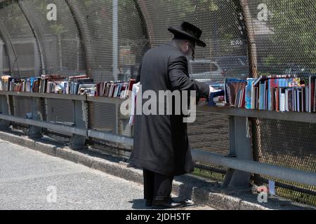 Ein anonymer orthodoxer jüdischer Mann mit Peyus & airpods stösst bei einem Verkauf religiöser Bücher im Freien nach. An der Lee Avenue in Williamsburg, Brooklyn, NYC Stockfoto