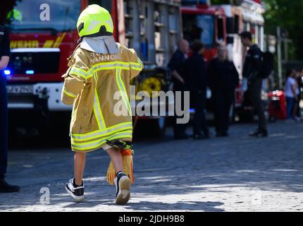 Hannover, Deutschland. 21.. Juni 2022. Ein Kind läuft beim Tag der deutschen Feuerwehrleute 29. in der viel zu großen Kleidung eines Feuerwehrleuten über den Trammplatz. Quelle: Julian Stratenschulte/dpa/Alamy Live News Stockfoto