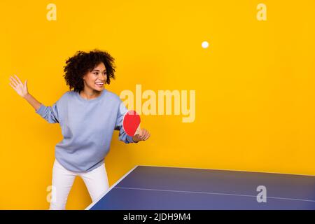 Foto von ziemlich süß gewellt Dame tragen blauen Sweatshirt lächelnd spielen Tischtennis isoliert gelben Hintergrund Stockfoto