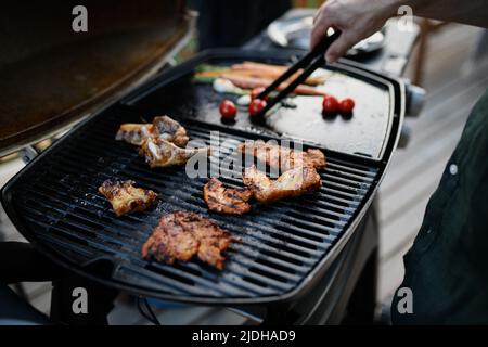 Nicht erkennbarer Mann, der während der Sommergartenparty der Familie Fleisch und Gemüse auf dem Grill grillt, Nahaufnahme Stockfoto