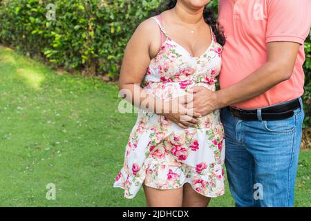 Mann berührt den Bauch seiner Schwangeren, während sie zusammen im Hof ihres Hauses sind Stockfoto