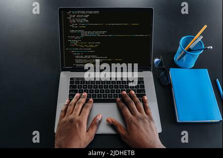 Draufsicht auf männliche afroamerikanische Hände auf einer Laptop-Tastatur sitzt DER IT-Spezialist, Programmierer, in einem modernen Büro und arbeitet an der Entwicklung einer Website, einer Anwendung, dem Schreiben von Codes und Datencode Stockfoto