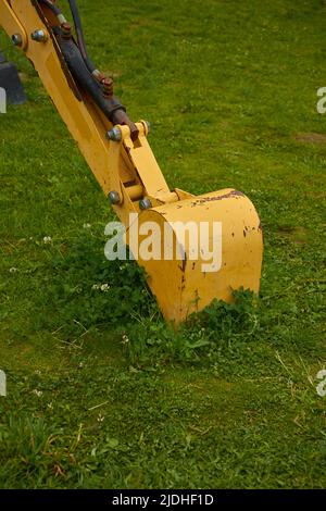 Der Eimer des gelben Baggers liegt auf dem Rasen Stockfoto
