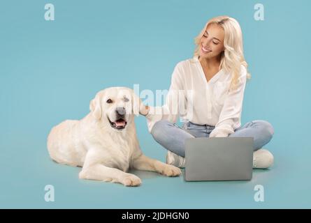 Porträt von niedlichen goldenen Retriever in der Nähe der Besitzerin liegen, Dame streicheln ihren Hund, mit Laptop-Computer, blauer Hintergrund Stockfoto