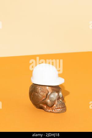 Totenkopf mit weißem Schutzhelm auf orangefarbenem Hintergrund. Schutzzubehör für Bauarbeiter. Halloween oder Santa Muerte Konzept mit Kopie-SPAC Stockfoto