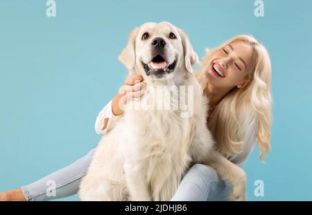 Haustiere und Menschen Konzept. Glückliche junge Dame posiert mit ihrem entzückenden goldenen Retriever Hund, der auf blauem Hintergrund sitzt Stockfoto