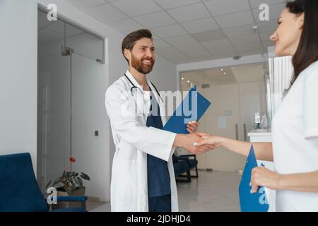 Zwei Ärzte in Uniform schüttelten die Hände und standen in der Klinikhalle in der Nähe der Rezeption Stockfoto
