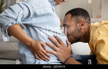 Kurzer Schuss des afroamerikanischen Mannes, der den Bauch seiner Frau küssen wird Stockfoto