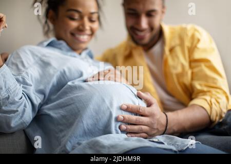 Schwarze Ehegatten erwarten Baby, Ehemann berührt Schwangeren Frau Bauch Indoor Stockfoto