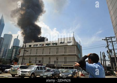 Manila, Philippinen - 11. Juli 2013: Der Mensch deutet auf großen Rauch, der hinter einem Gebäude in Makati City herkommt. Das Feuer brannte Hunderte von Shanties nieder. Stockfoto