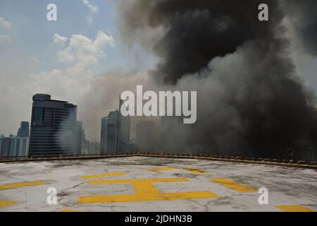 Manila, Philippinen - 11. Juli 2013: Großer grauer Rauch erreicht die Spitze eines hohen Gebäudes mit einem Hubschrauberlandeplatz im Finanzviertel von Makati City. Stockfoto