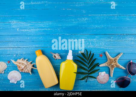 Flache Lay-Komposition mit Sonnencreme und Muscheln auf blauem Holzhintergrund. Stockfoto