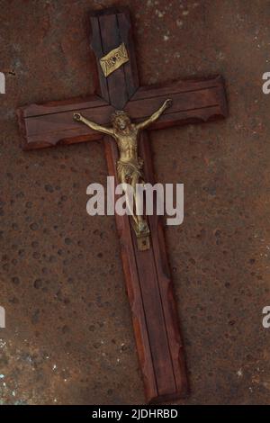 Hölzernes Kruzifix mit Messingfigur von Jesus darauf liegend auf rostigem Blech Stockfoto