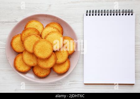 Hausgemachte Butterkurzbrote auf einem rosafarbenen Teller, leerer Notizblock, Draufsicht. Flach liegend, über Kopf, von oben. Stockfoto