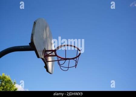Basketballkorb und -Brett aus Metall gegen einen wolkenlosen, starken blauen Himmel mit Kopierfläche. Beleuchtet mit angestrahltem Sonnenlicht. Stockfoto
