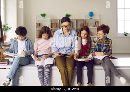 Schüler und Lehrer sitzen im Klassenzimmer auf dem Schreibtisch, lesen Bücher und machen Notizen Stockfoto